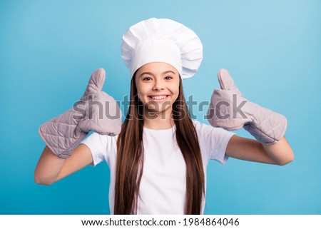 Photo of cheerful positive happy little lady wear chef hat gloves make thumbs-up isolated on blue color background