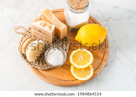 Eco friendly natural cleaners, jar with baking soda, dish brush, lemon, soap on white marble table background. Organic ingredients for homemade cleaning. Zero waste concept.