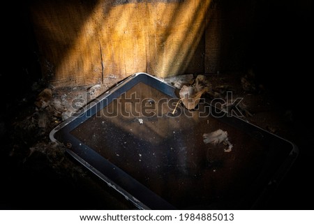 tablet on a pile of dirt and dust against the background of old walls made of hewn boards in a beam of light