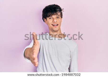 Handsome hipster young man wearing casual white shirt smiling friendly offering handshake as greeting and welcoming. successful business. 