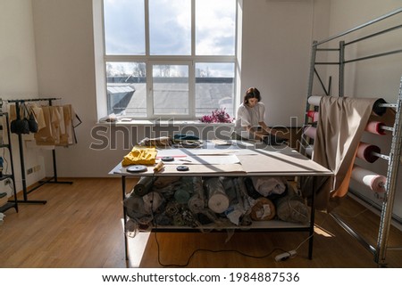 Woman tailor work with fabric on table in workshop studio. Creative clothes designer measure cloth for new collection in atelier. Busy female seamstress with textile. Dressmaker trendy creative space