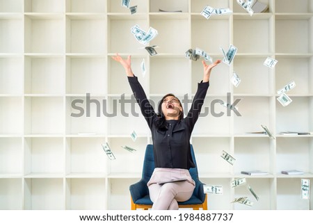 Young happy woman winner throwing money banknotes, working from home throwing money over her head. Happy Smiling woman throws the money up in the air and sitting on chair at home

