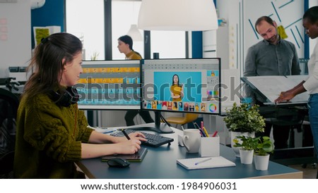 Retoucher woman working on computer with two monitors and stylus pencil in photo editing software sitting in creative agency office. Graphic editor retouching photos of client in professional app