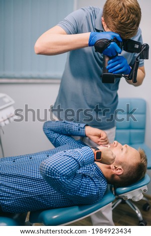 A dentist takes a picture of a patient's teeth using a camera in his office. Medium shot.