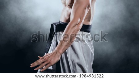 Composition of midsection of male martial artist with black belt over clouds of smoke. sports and competition concept digitally generated image.