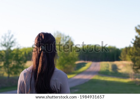 Young woman looking up the road ahead of her at sunset Royalty-Free Stock Photo #1984931657