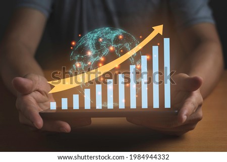 A man holding the smart tablet and watching analysis business grow graph and arrow, global and computer light economic and success concept Royalty-Free Stock Photo #1984944332