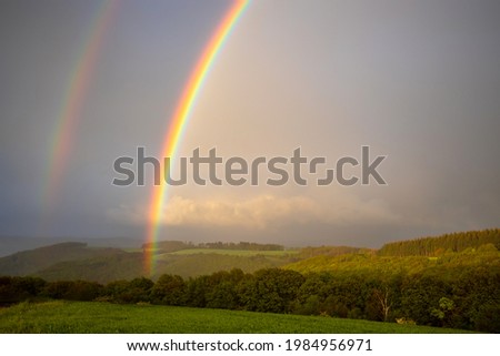 a beautiful partial rainbow on the blue sky above the green field and trees
