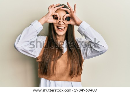 Beautiful brunette young woman wearing casual clothes doing ok gesture like binoculars sticking tongue out, eyes looking through fingers. crazy expression. 