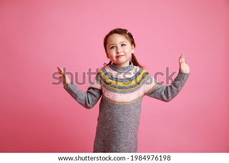 Portrait of little funny smiling girl in warm dress on rosa background.