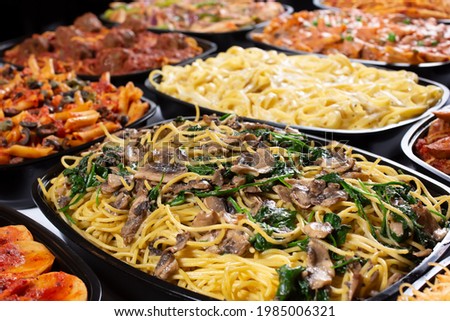 A view of several varieties of pasta trays, featuring a tray of mushroom and spinach spaghetti.