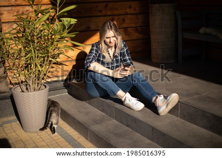 Young woman siting on steps on porch on summer day and uses mobile phone for text message