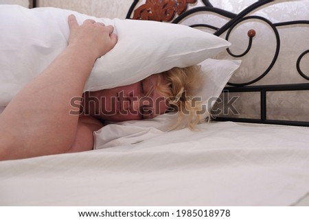 The woman lies in bed and covers her head with a pillow.
