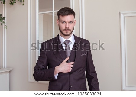 beautiful young man with a beard brunette model. guy in a classic suit in a light stylish interior. groom. portrait