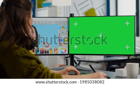 Creative woman retoucher editing assets in digital retouching program, working concentrated in photo production studio looking in computer with green screen, chroma key mockup isolated display.