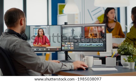 Videographer in web online conference with project manager on video call editing client work, getting feedback on commercial movie using post production software on two monitors in start up office