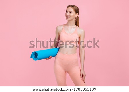 Go to gym, Sportive young woman in a sports top and leggings, with a fitness mat on a pink background, sports and healthy lifestyle