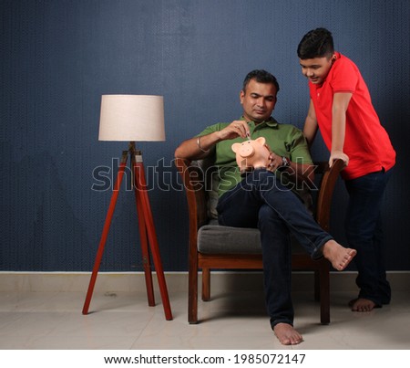 Father's day or finance education concept - Indian father teaching importance of saving to his son at home with piggy bank Royalty-Free Stock Photo #1985072147