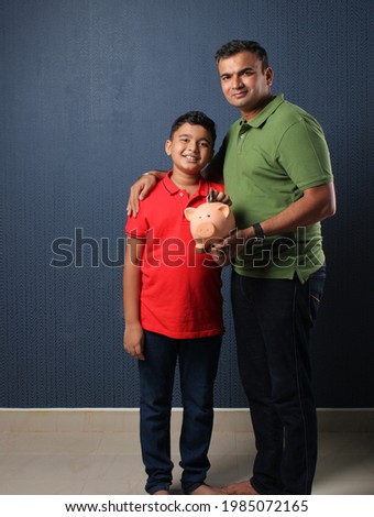 Father's day or finance education concept - Indian father teaching importance of saving to his son at home with piggy bank Royalty-Free Stock Photo #1985072165