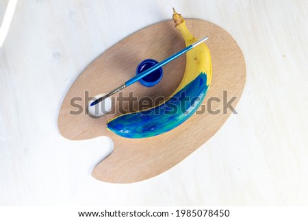 banana fruit colored with blue paint by brush on artist palette 