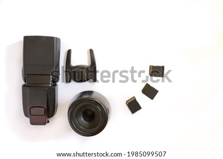 Photographic equipment showing a black speedlite flash together with a fflash stand, a zoom lens and three sd memory cards. White background. Copy space. Concept of digital photography.