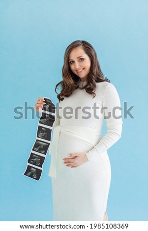 Pretty 20-week pregnant woman with ultrasound scan image on blue background, 