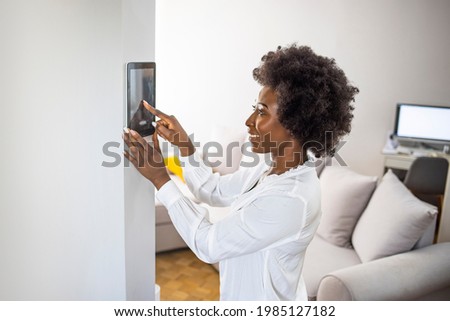 Young african girl woman lady adjusting remote climate control panel settings wall touch screen set heating conditioning switch on security system energy saving mode, black lady use smart home concept Royalty-Free Stock Photo #1985127182