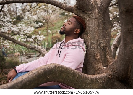 Man leaning on the tree with closed eyes and resting at the nature