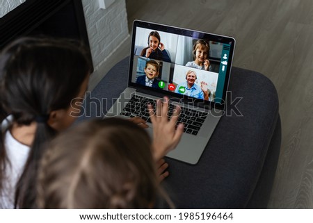 Little girls at home with laptop, video chatting with their friends.