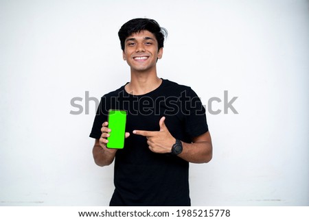 Young indian boy holding a mobile phone and point towards it's screen. Mobile phone with a green screen for mockup.