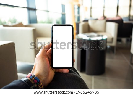 (Copy space) Overhead view of an human hand holding a smart phone with a white screen in an airport lounge. Concept of showing information on a mobile phone during Covid-19 pandemic. 