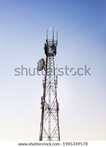 A large communications tower in rural Australia, with a daytime picture of the moon located between the twin aerials at the top.