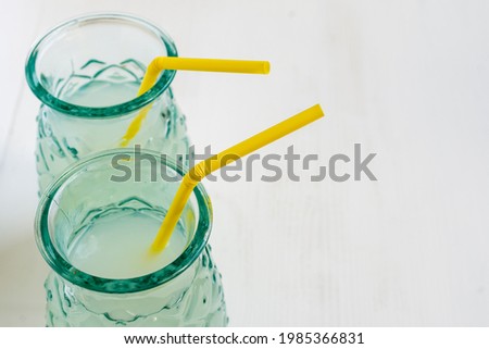 Top view of two glasses with lemon juice with yellow straw, selective focus, on white table, horizontal, with copy space