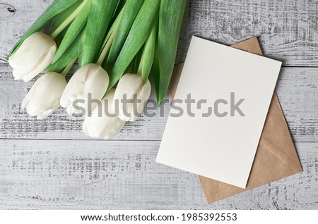 Greeting card mockup with envelope and tulip flowers bouquet on wooden background, top view, copy space