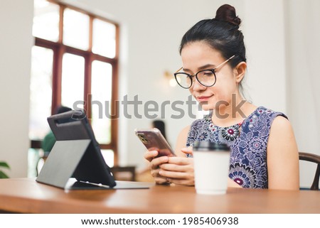 Young beautiful woman using smartphone and tablet in coffee shop. Asian female in glasses working with devices in cafe. 