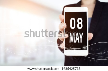 May 8th. Day 8 of month, Calendar date. White smartphone with Calendar date in businesswoman hand on blurred background. Spring month, day of the year concept