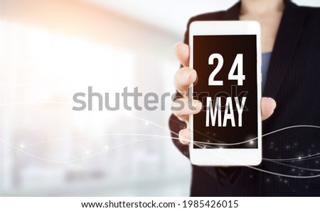 May 24th. Day 24 of month, Calendar date. White smartphone with Calendar date in businesswoman hand on blurred background. Spring month, day of the year concept