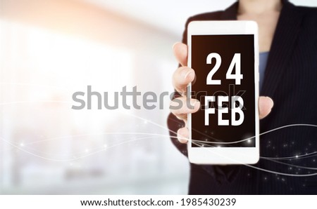 February 24th. Day 24 of month, Calendar date. White smartphone with Calendar date in businesswoman hand on blurred background. Winter month, day of the year concept