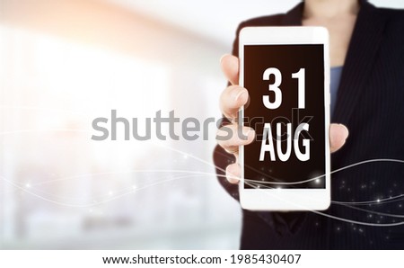 August 31st . Day 31 of month, Calendar date. White smartphone with Calendar date in businesswoman hand on blurred background. Summer month, day of the year concept