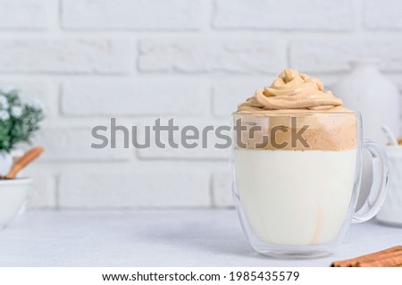 A glass mug with Dalgona coffee on light background with copy space. Korean drink Milo Dalgona with cinnamon. Milk with frothy whispered creamy coffee foam on top.