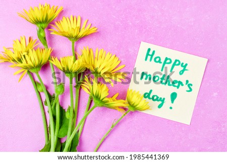 The inscription on the note sheet "happy mother's day" and a bouquet of yellow daisies on a bright pink background.