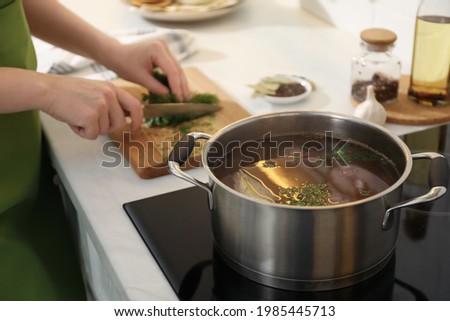 Homemade bouillon recipe. Woman cutting greenery in kitchen, focus on pot