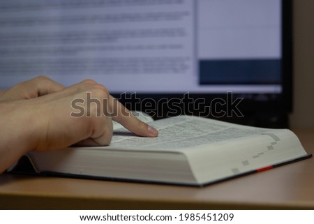 Closeup of a translator working with CAT (Computer-Assisted Translation) tool and dictionary. Royalty-Free Stock Photo #1985451209