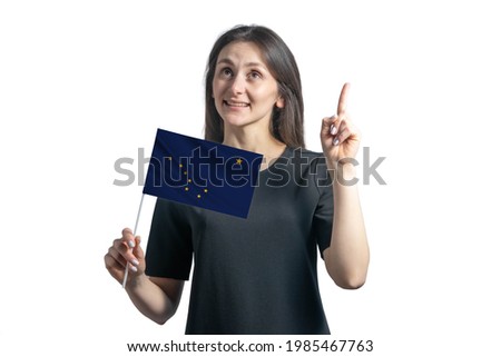Happy young white woman holding flag of Alaska and points thumbs up isolated on a white background.