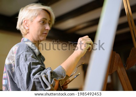Cinematic shot of female creative artist painter concentrated and inspired painting picture with paint brush and oil colors on canvas. High quality photo
