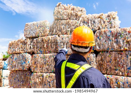 An employee at a recycling plant is pointing to plastic waste being sent to the recycling process. Royalty-Free Stock Photo #1985494967