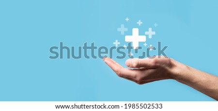 Male hand holding plus icon on blue background. Plus sign virtual means to offer positive thing like benefits, personal development, social network Profit,health insurance, growth concepts. Royalty-Free Stock Photo #1985502533