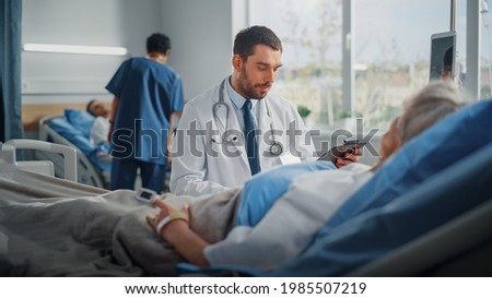Hospital Ward: Friendly Doctor Talks to Beautiful Senior Female Patient Resting in Bed, Explains Test Results, Gives Recovery Advice. Physician Talks to Old Lady Recovering after Successful Surgery Royalty-Free Stock Photo #1985507219