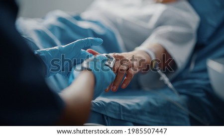 Hospital Ward: Senior Female Resting in a Bed Nurse Has Finger Heart Rate Monitor Pulse Oximeter showing Pulse. Anonymous Nurse Checks Vitals of Woman Getting well after Surgery.