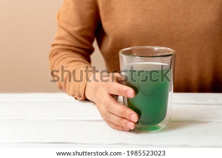 Woman hand holding cup of chlorophyll water on white table Royalty-Free Stock Photo #1985523023